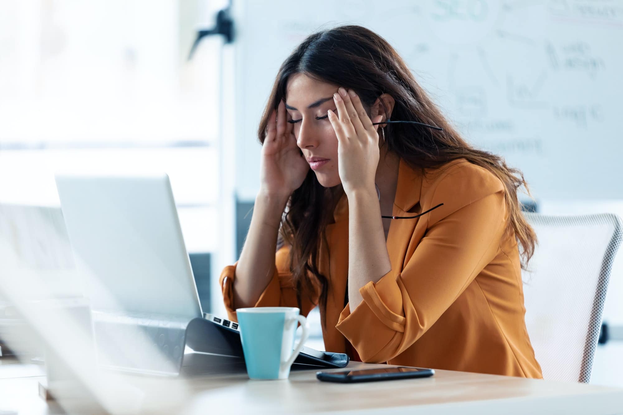 Mujer joven de negocios con dolor de cabeza que trabaja con el ordenador portátil en la oficina.
